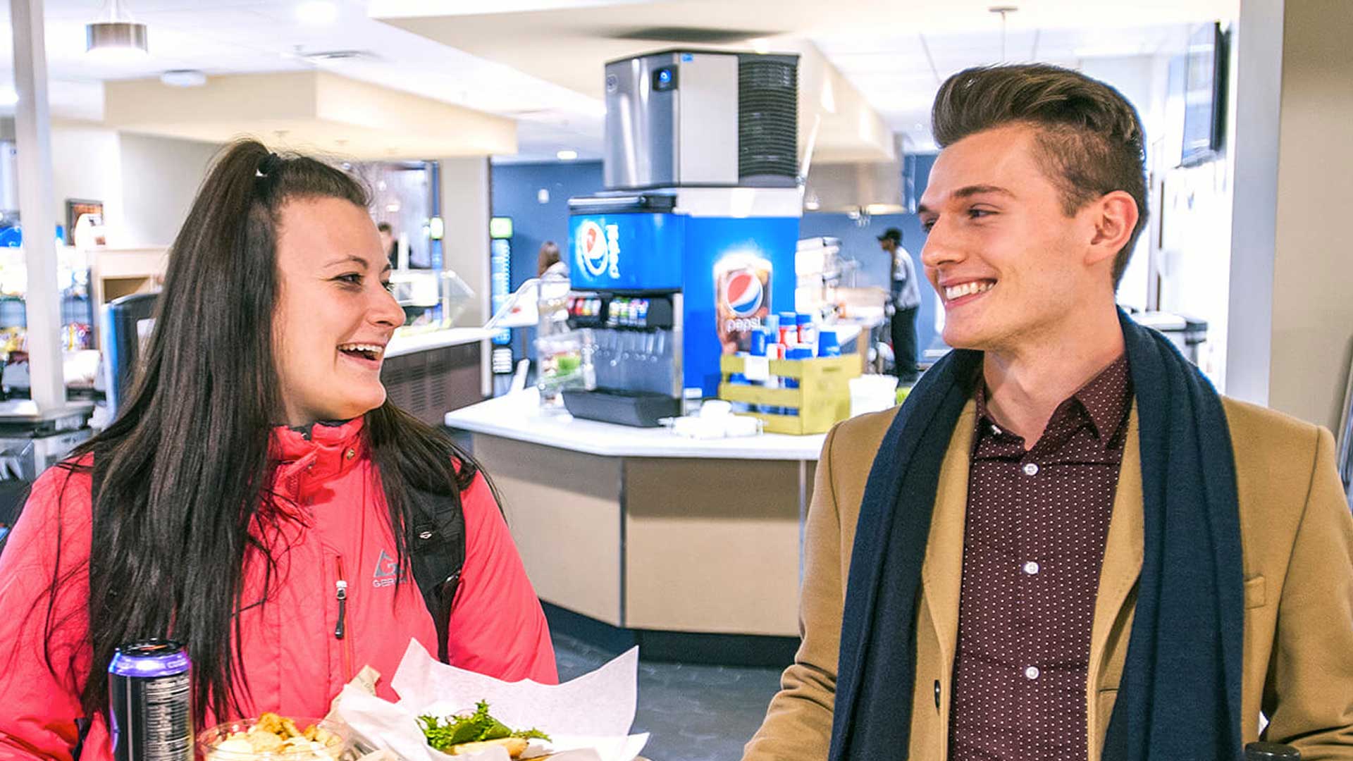 Two students smiling at each other while walking out of servery