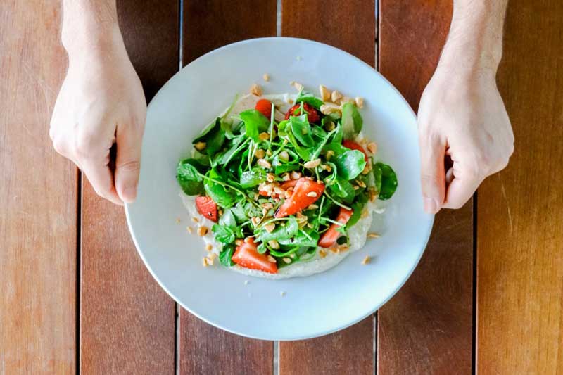 Hands holding plate of salad over table