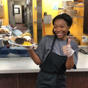 Girl smiling with thumbs up and plate of Haitian food in her other hand